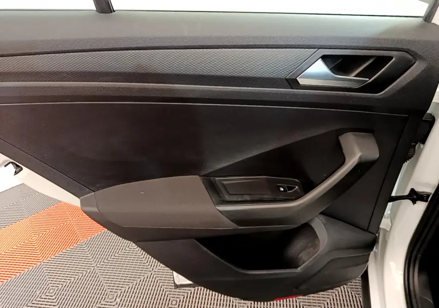 Vue rapprochée de la porte avant droite noire du Volkswagen T-Roc blanc, avec poignée et commande de vitre électrique.