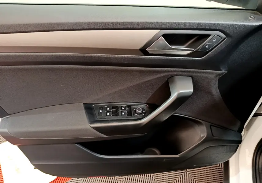 Vue rapprochée de la porte côté conducteur du Volkswagen T-Roc blanc, avec commandes électriques et poignée noire.