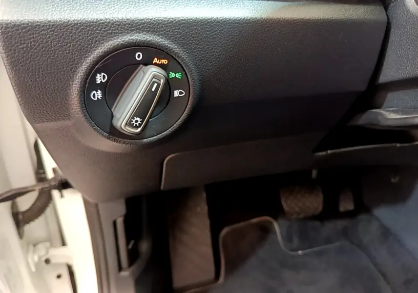 Gros plan sur le bouton de commande des phares dans l’habitacle noir du Volkswagen T-Roc blanc côté conducteur.