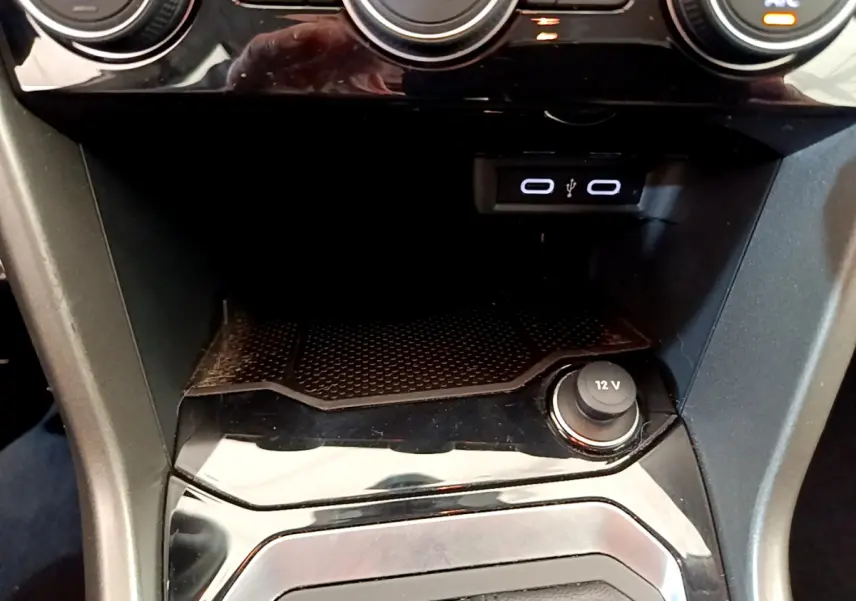 Vue rapprochée de la console centrale noire du Volkswagen T-Roc blanc, avec prise 12V et ports USB visibles.