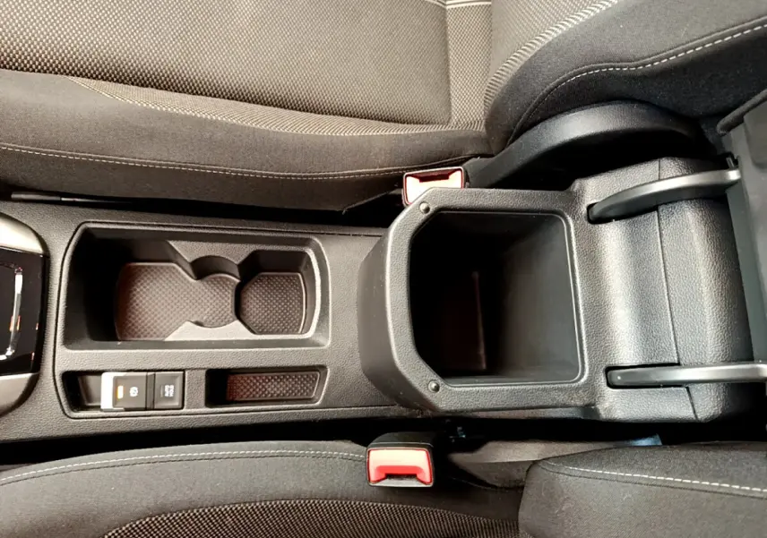 Vue plongeante sur la console centrale noire du Volkswagen T-Roc blanc, avec porte-gobelets et frein à main électrique.