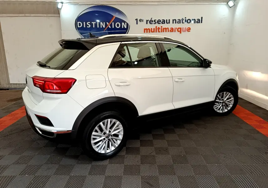 Volkswagen T-Roc blanc en 3/4 arrière droit, toit noir contrasté et jantes alliage dans showroom intérieur.