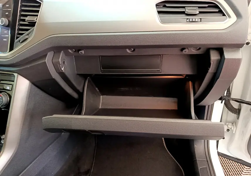Gros plan sur la boîte à gants ouverte côté passager du Volkswagen T-Roc blanc, tableau de bord moderne visible.