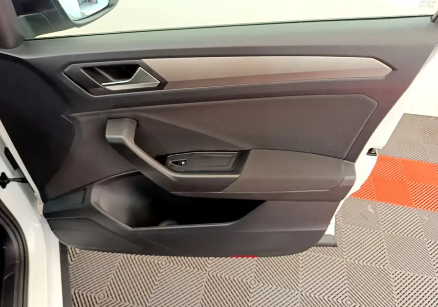 Porte côté conducteur ouverte d’un Volkswagen T-Roc blanc, intérieur noir avec poignée et commande de vitre intégrée.
