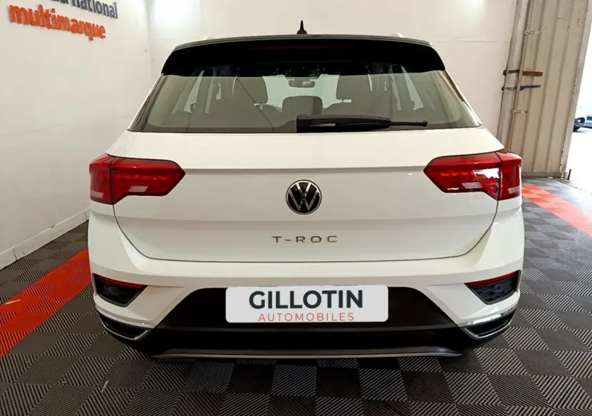 Vue arrière d'un Volkswagen T-Roc blanc avec feux arrière rouges et toit noir dans un garage.