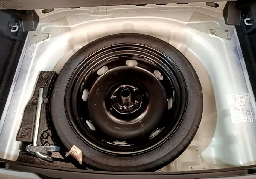 Roue de secours galette noire dans le coffre blanc d'un Volkswagen T-Roc 2021, avec outils de changement visibles.
