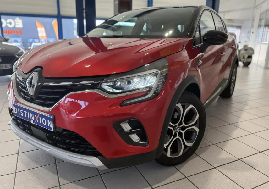 Vue 3/4 avant droit d’un Renault Captur rouge foncé avec jantes alliage et calandre chromée en showroom.