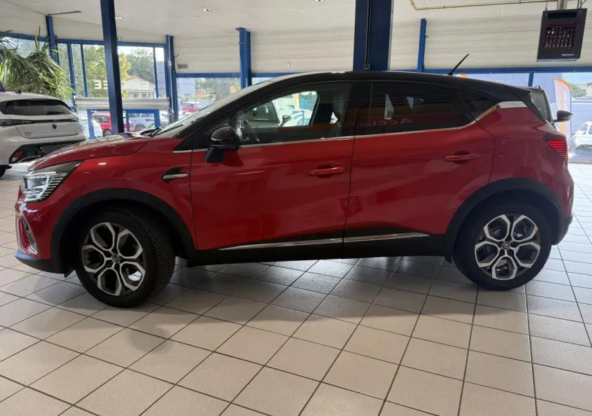 Profil côté gauche d'un Renault Captur 2020 rouge foncé avec jantes alliage et toit noir en showroom.