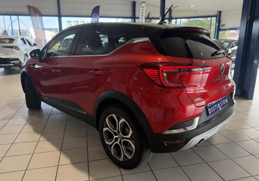 Vue 3/4 arrière droite d'un Renault Captur rouge foncé avec toit noir en showroom, soulignant ses feux arrière LED et jantes stylées.