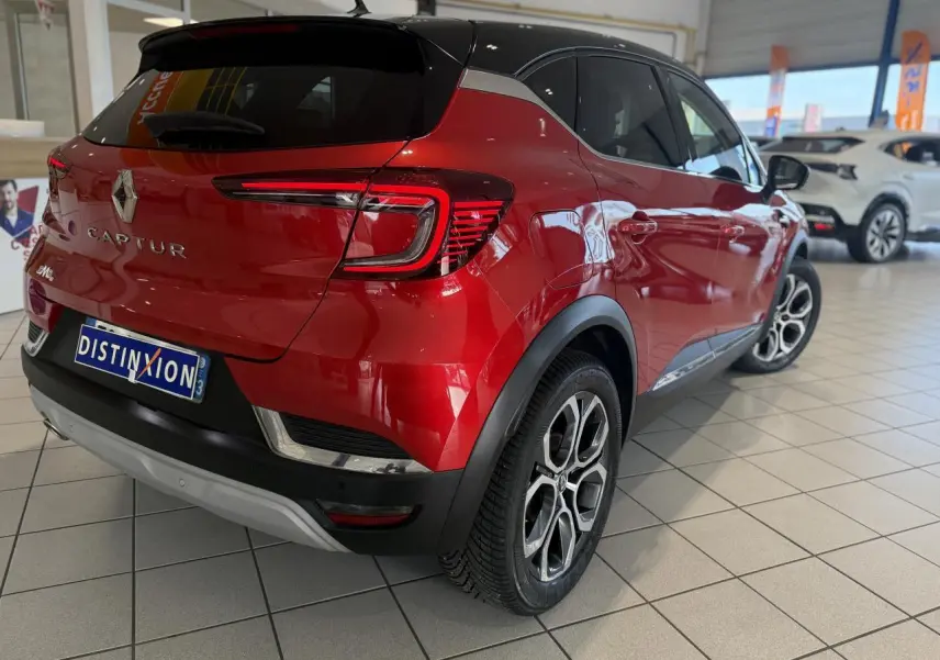 Vue 3/4 arrière droite d'un Renault Captur rouge foncé avec toit noir et jantes alliage en concession.