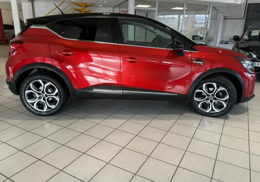 Profil droit du Renault Captur 2020 rouge foncé avec toit noir et jantes alliage en showroom.