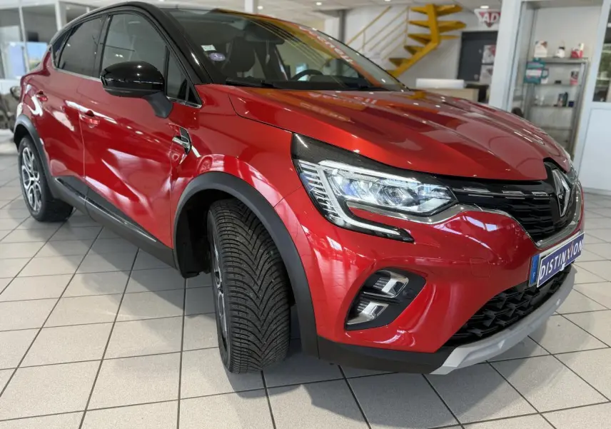 Renault Captur rouge foncé en 3/4 avant droit, avec phares allumés et jantes alliage visibles en showroom.
