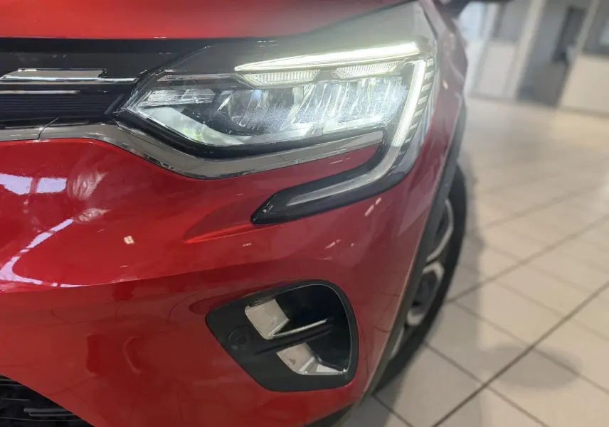 Gros plan sur le phare avant droit et le pare-chocs rouge foncé d'un Renault Captur 2020 en showroom.