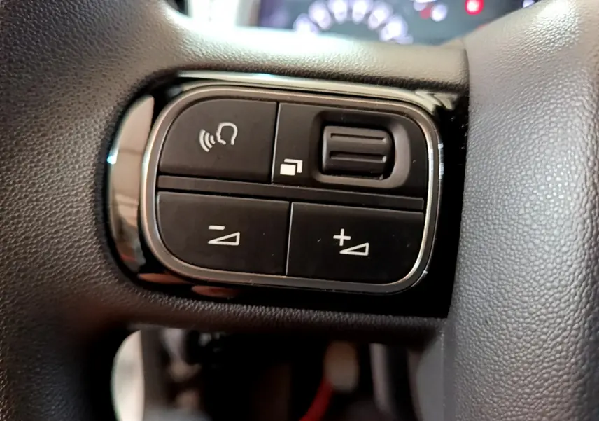 Gros plan sur les commandes noires du volant de la Citroën C3 PureTech 68 BVM Live, avec boutons de volume et appel.
