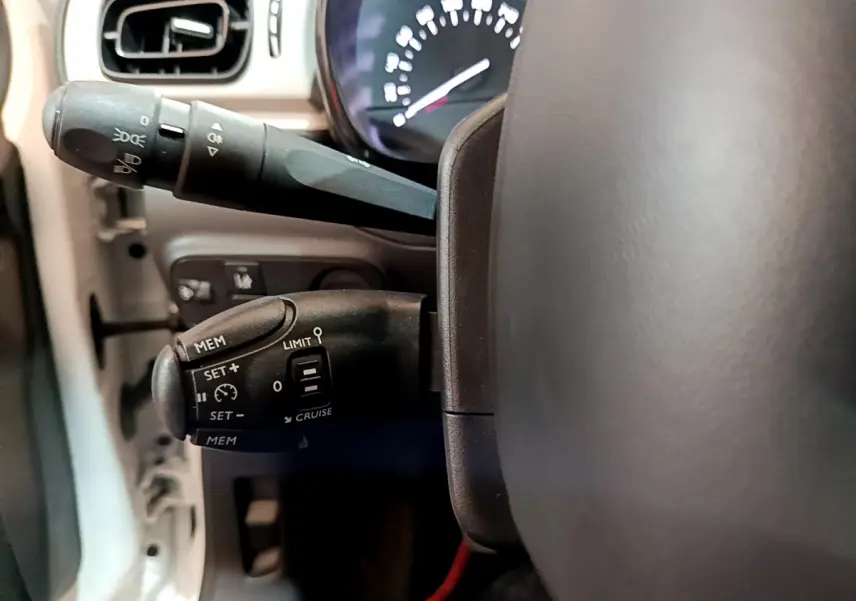 Gros plan sur les commandes du régulateur de vitesse et des phares à gauche du volant d'une Citroën C3 blanche de 2018.