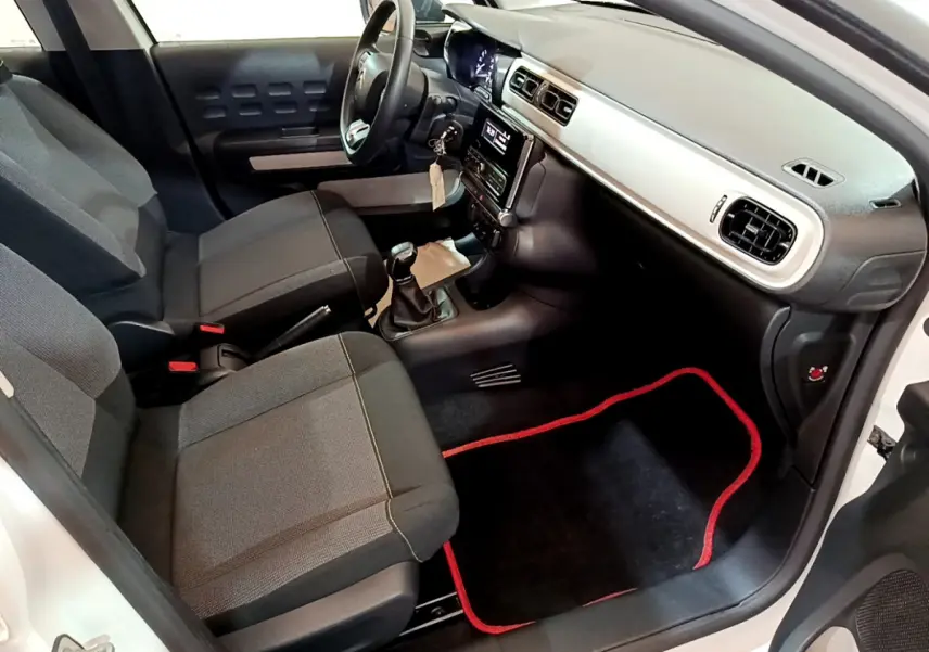 Vue intérieure côté passager avant de la Citroën C3 blanche, montrant sièges gris et tableau de bord avec console centrale.