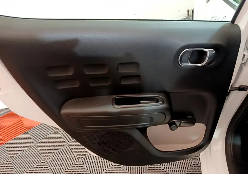 Vue intérieure de la porte avant gauche blanche d'une Citroën C3 2018 avec poignée chromée et commande de vitre manuelle.