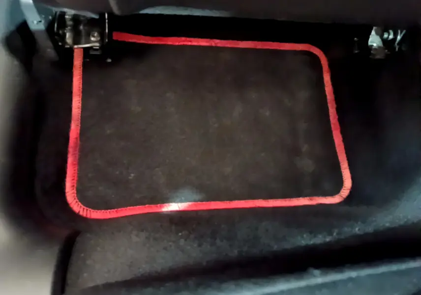 Gros plan sur le tapis de sol noir avec bordure rouge dans l'habitacle d'une Citroën C3 blanche.