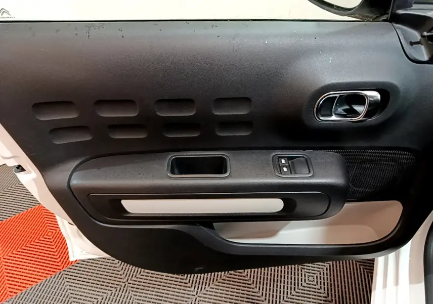 Vue rapprochée de la porte avant gauche blanche de la Citroën C3 2018 avec poignée intérieure chromée et boutons de fenêtre.