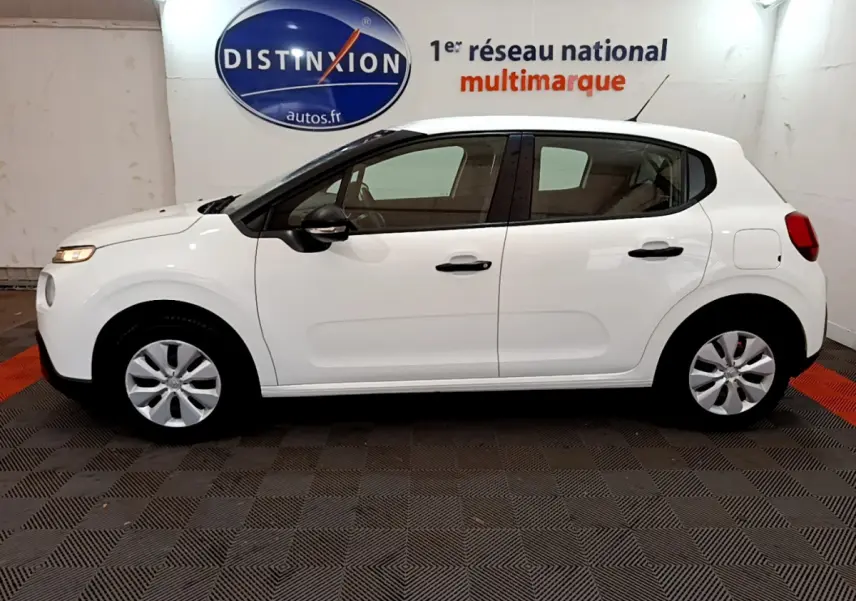 Vue de profil côté gauche d'une Citroën C3 blanche de 2018, avec poignées et rétroviseurs noirs, stationnée en intérieur.