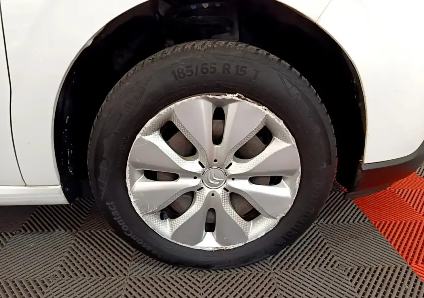 Gros plan sur la roue avant droite d'une Citroën C3 blanche, jante avec enjoliveur endommagé visible.
