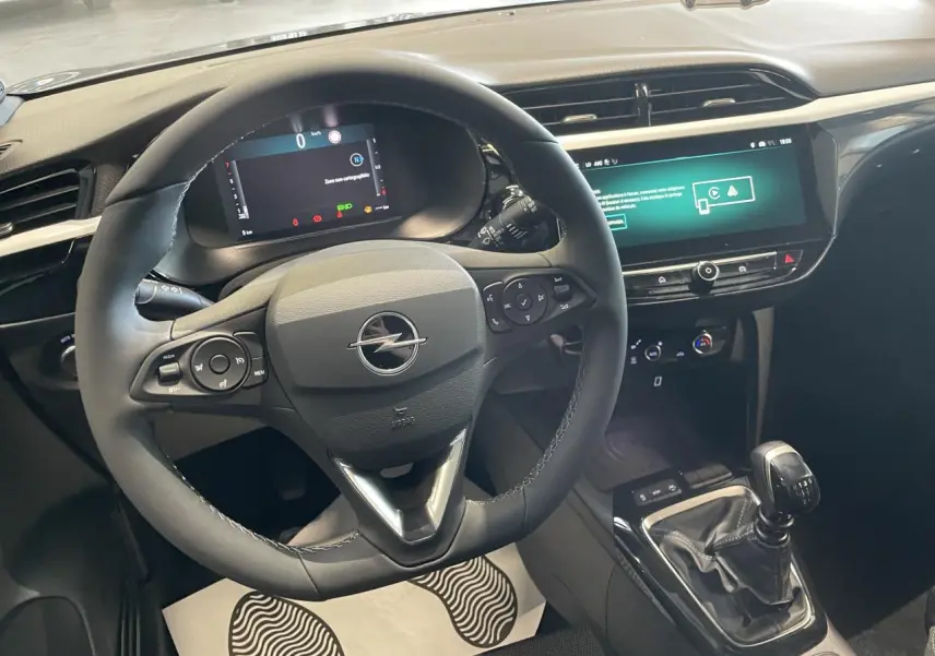 Vue intérieure centrée sur le volant noir et la console centrale avec levier de vitesse manuelle de l'Opel Corsa gris.