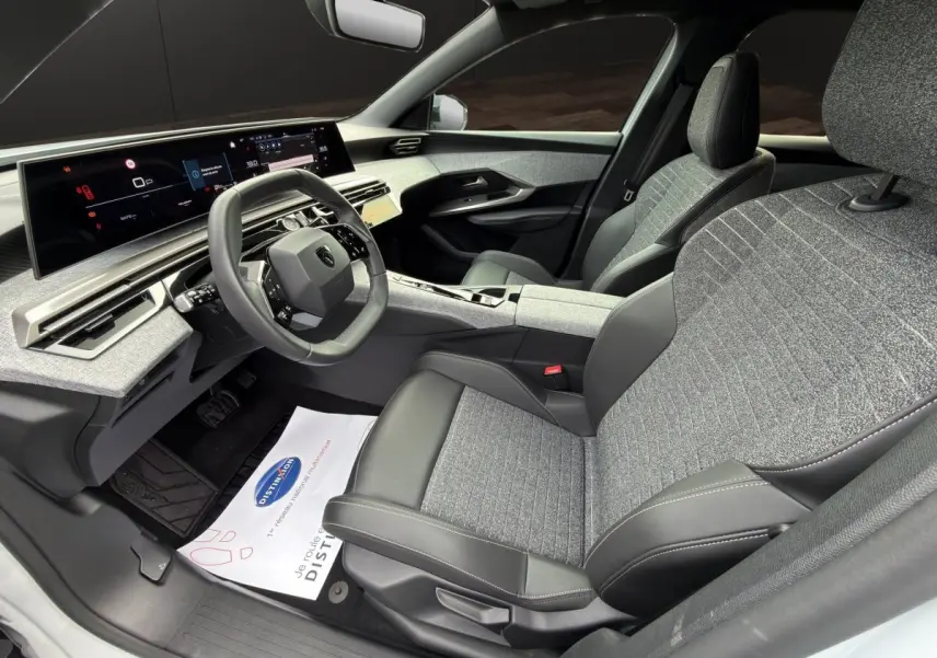 Vue intérieure côté conducteur du Peugeot 3008 2025, montrant le volant cuir multifonctions et les sièges bi-matière gris et noir.