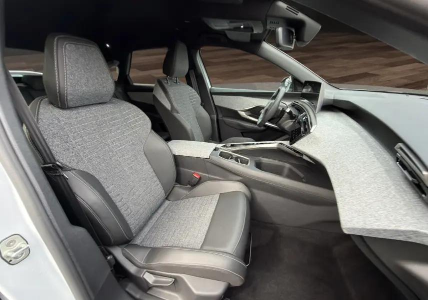 Vue intérieure côté conducteur du Peugeot 3008 blanc 2025, sièges tissu et cuir gris, tableau de bord moderne texturé clair.