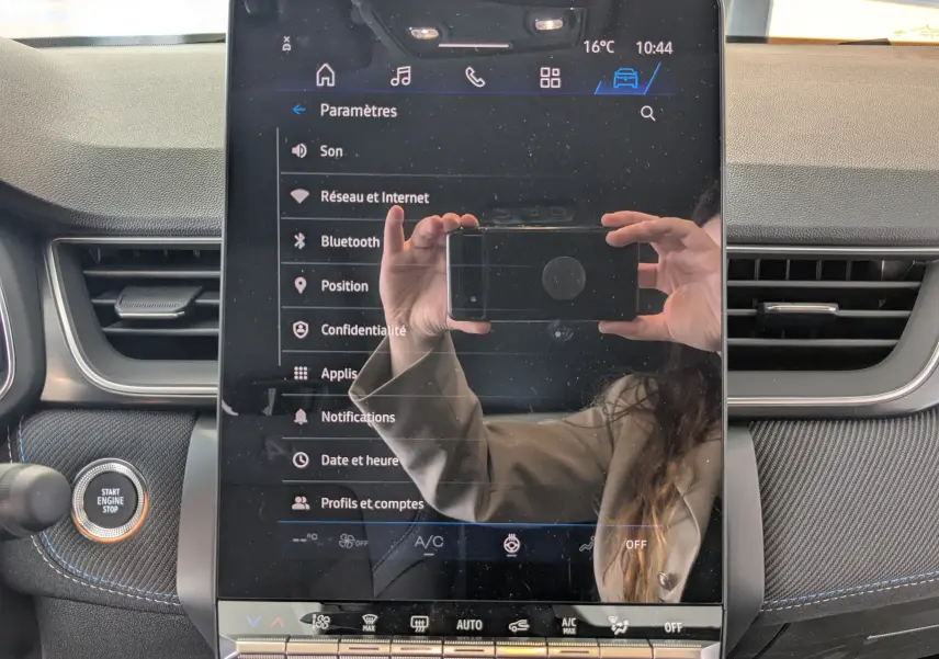 Écran tactile central du tableau de bord du Renault Symbioz bleu Iron, avec menu paramètres affiché et reflet du photographe.