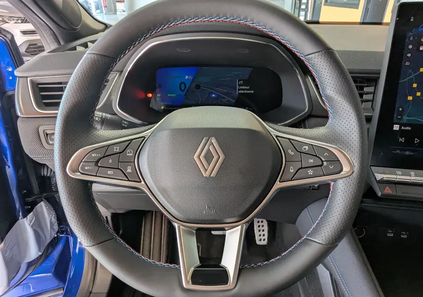 Vue frontale du volant noir perforé avec surpiqûres tricolores du Renault Symbioz Bleu Iron, tableau de bord digital en arrière-plan.