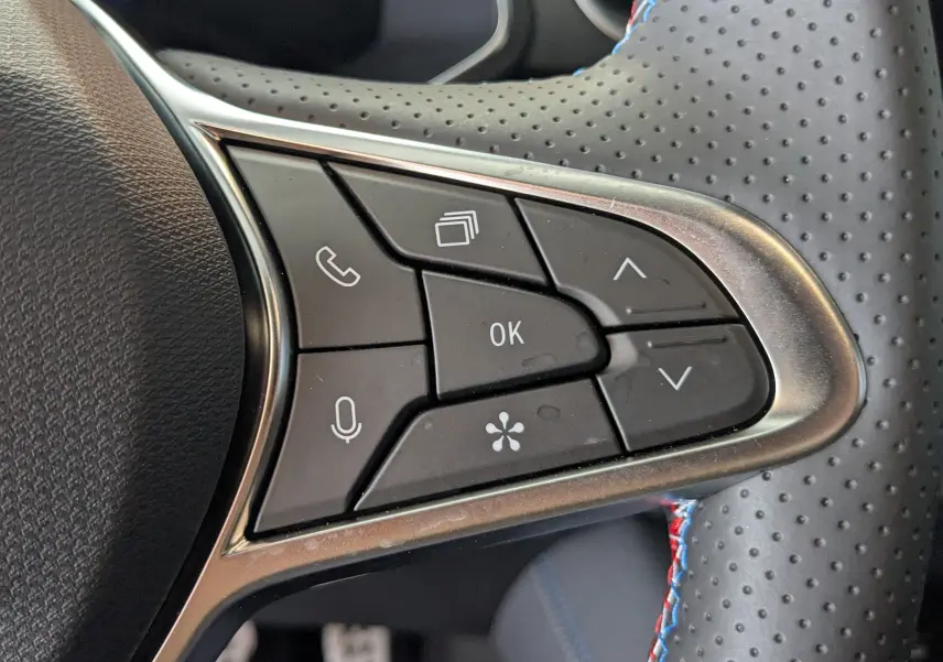 Gros plan sur les commandes multifonctions au volant perforé du Renault Symbioz bleu Iron, version hybride 2025.