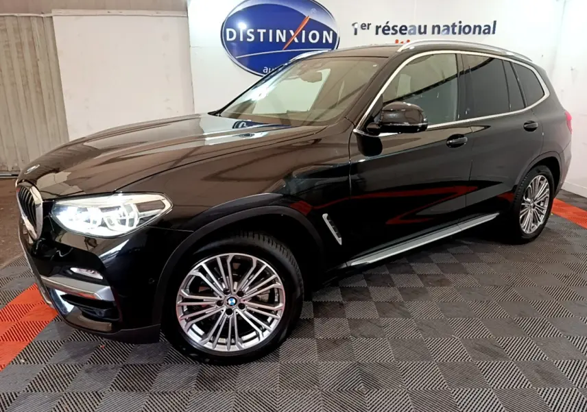 BMW X3 xDrive20d noir en 3/4 avant droit avec jantes alliage et phares LED allumés en intérieur showroom.