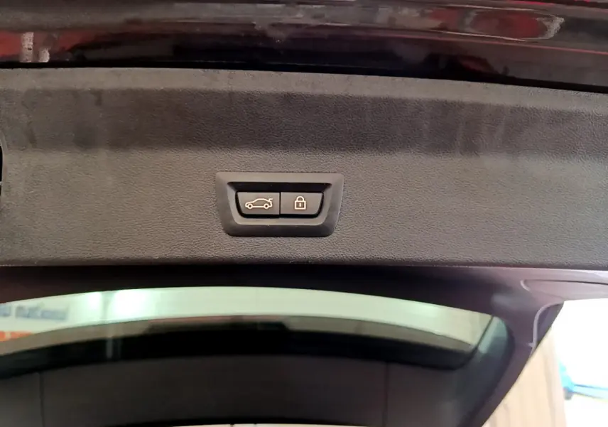 Bouton de fermeture et verrouillage du coffre sur le hayon intérieur d’un BMW X3 noir, vue en contre-plongée.