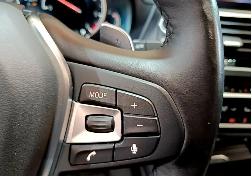 Gros plan sur les commandes du volant en cuir noir d'une BMW X3 2019, boutons mode, volume et téléphone visibles.