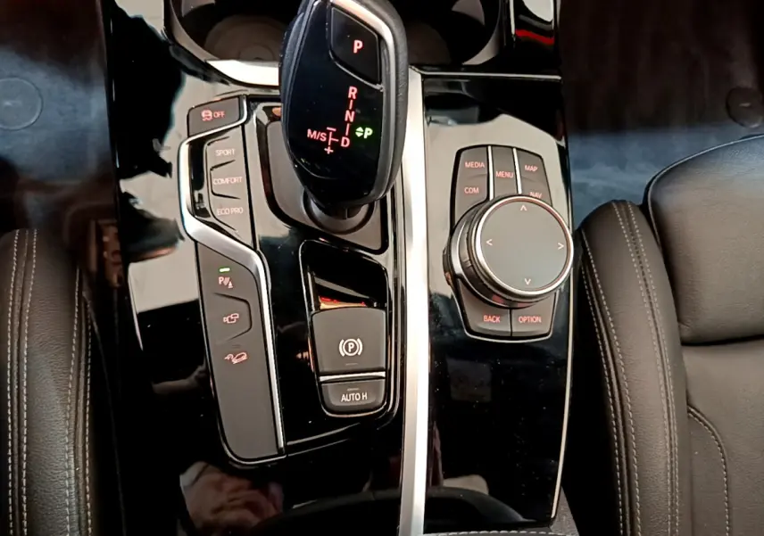 Gros plan sur la console centrale noire brillante du BMW X3 2019 avec levier de vitesse automatique et molette de contrôle.
