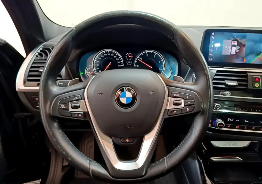 Vue frontale du volant en cuir noir et du tableau de bord digital d'une BMW X3 2019 avec écran tactile et affichage caméra.