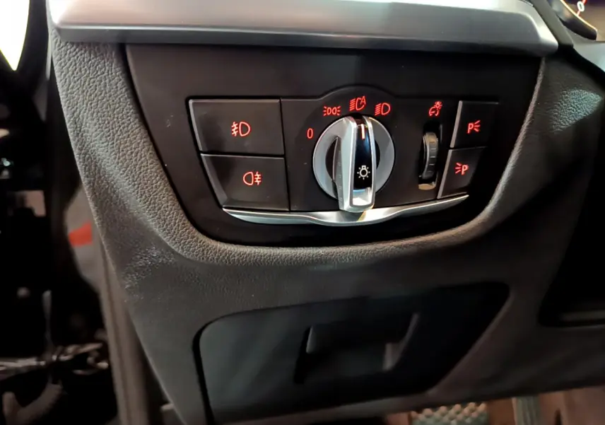 Gros plan sur le panneau de commande des phares avec éclairage rouge dans l'habitacle noir du BMW X3 xDrive20d 2019.