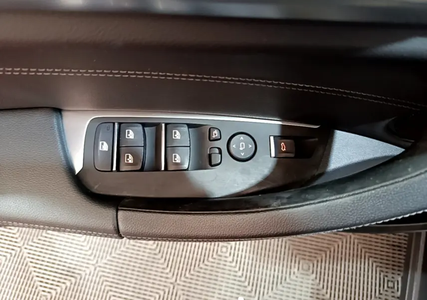 Vue rapprochée des commandes de lève-vitres et rétroviseurs sur la porte côté gauche d’un BMW X3 noir.