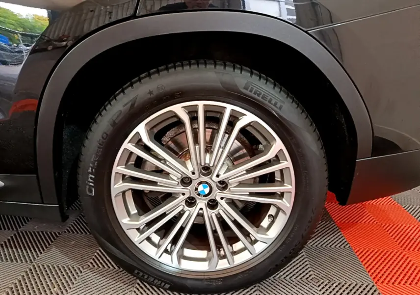 Gros plan sur la roue avant droite d’un BMW X3 noir, jante alliage multi-branches et pneu Pirelli visible.