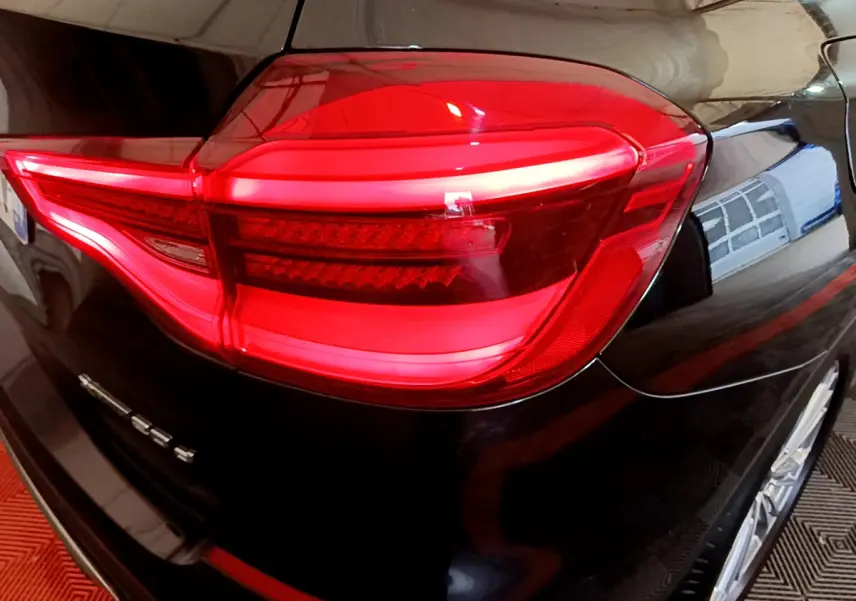 Gros plan sur le feu arrière droit rouge d’un BMW X3 noir, version xDrive20d, avec reflet du garage visible.