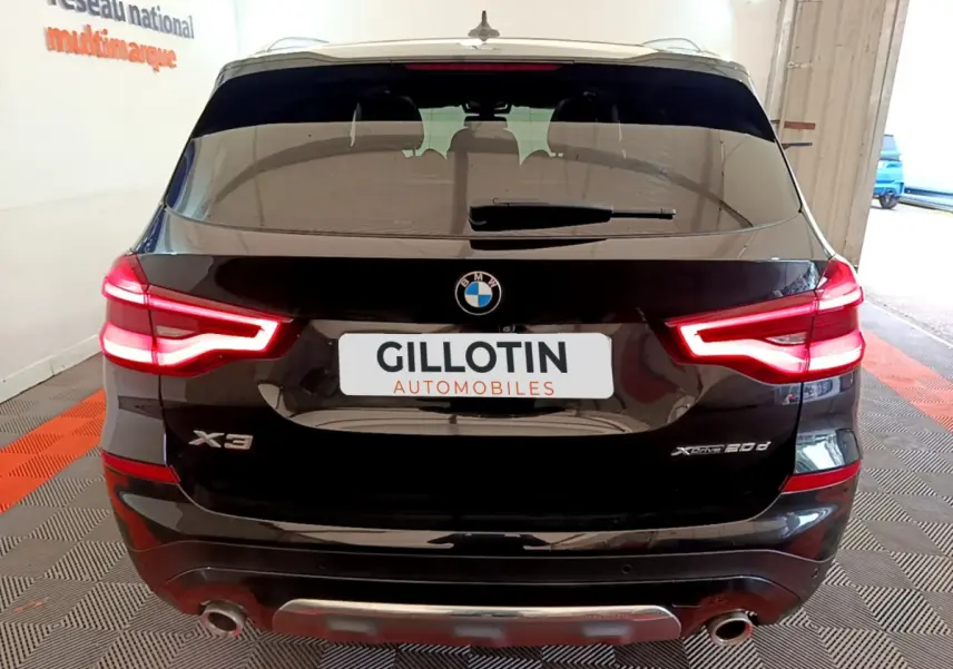 Vue arrière d'un BMW X3 noir avec feux LED allumés et double sortie d'échappement visible en intérieur showroom.