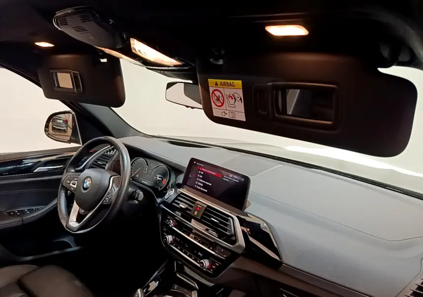 Vue intérieure avant gauche du BMW X3 noir de 2019, avec tableau de bord moderne et écran tactile central allumé.