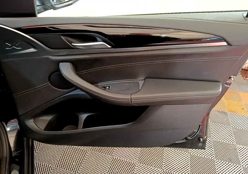 Gros plan sur la porte intérieure côté gauche noire du BMW X3 2019 avec surpiqûres blanches et poignée intégrée.