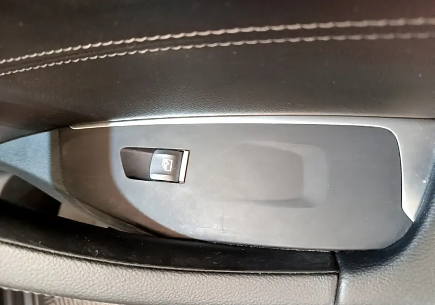 Gros plan sur le bouton de commande de la vitre électrique côté conducteur, entouré de garniture noire et coutures blanches.