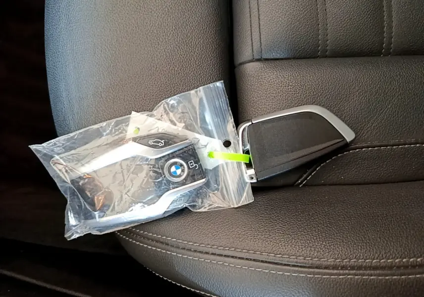 Clé BMW noire dans un sachet plastique posée sur un siège en cuir noir, vue rapprochée intérieure.