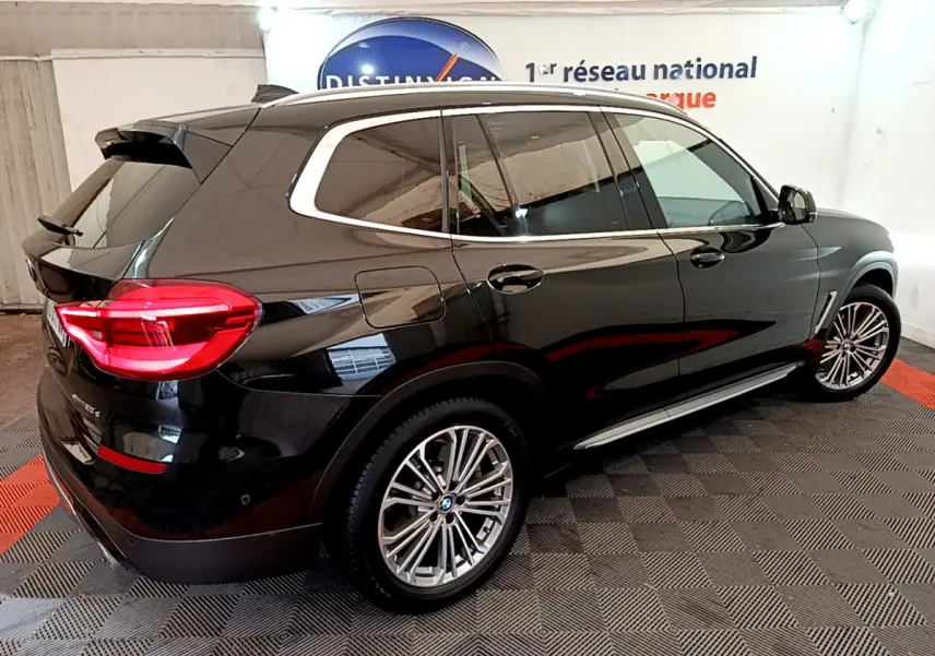 BMW X3 xDrive20d noir vue 3/4 arrière côté droit, avec jantes alliage et feux arrière LED allumés.