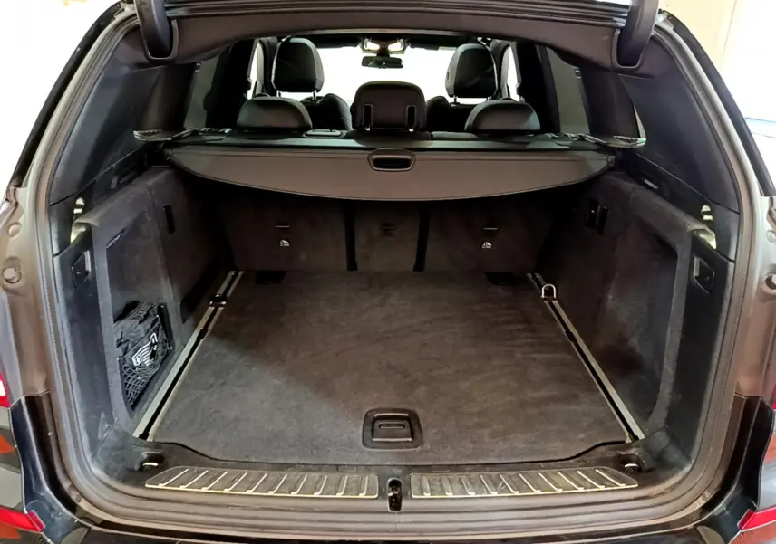 Coffre ouvert vu de l'arrière d'un BMW X3 noir, montrant un espace de chargement spacieux et tapis gris.