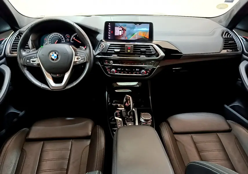 Vue intérieure avant de la BMW X3 2019, tableau de bord noir avec écran tactile et volant cuir multifonctions.