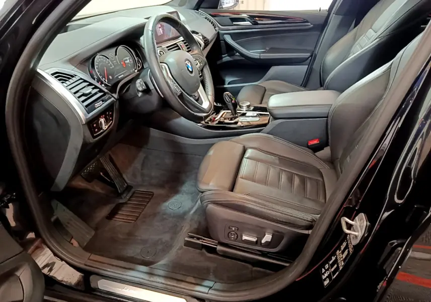 Vue intérieure côté conducteur d'une BMW X3 noire 2019, sièges cuir noirs et tableau de bord moderne avec commandes intégrées.