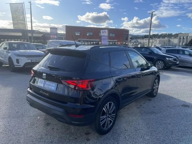 Vue 3/4 arrière droite d’un SEAT Arona noir 2023, avec feux arrière allumés, stationné en extérieur sur un parking.